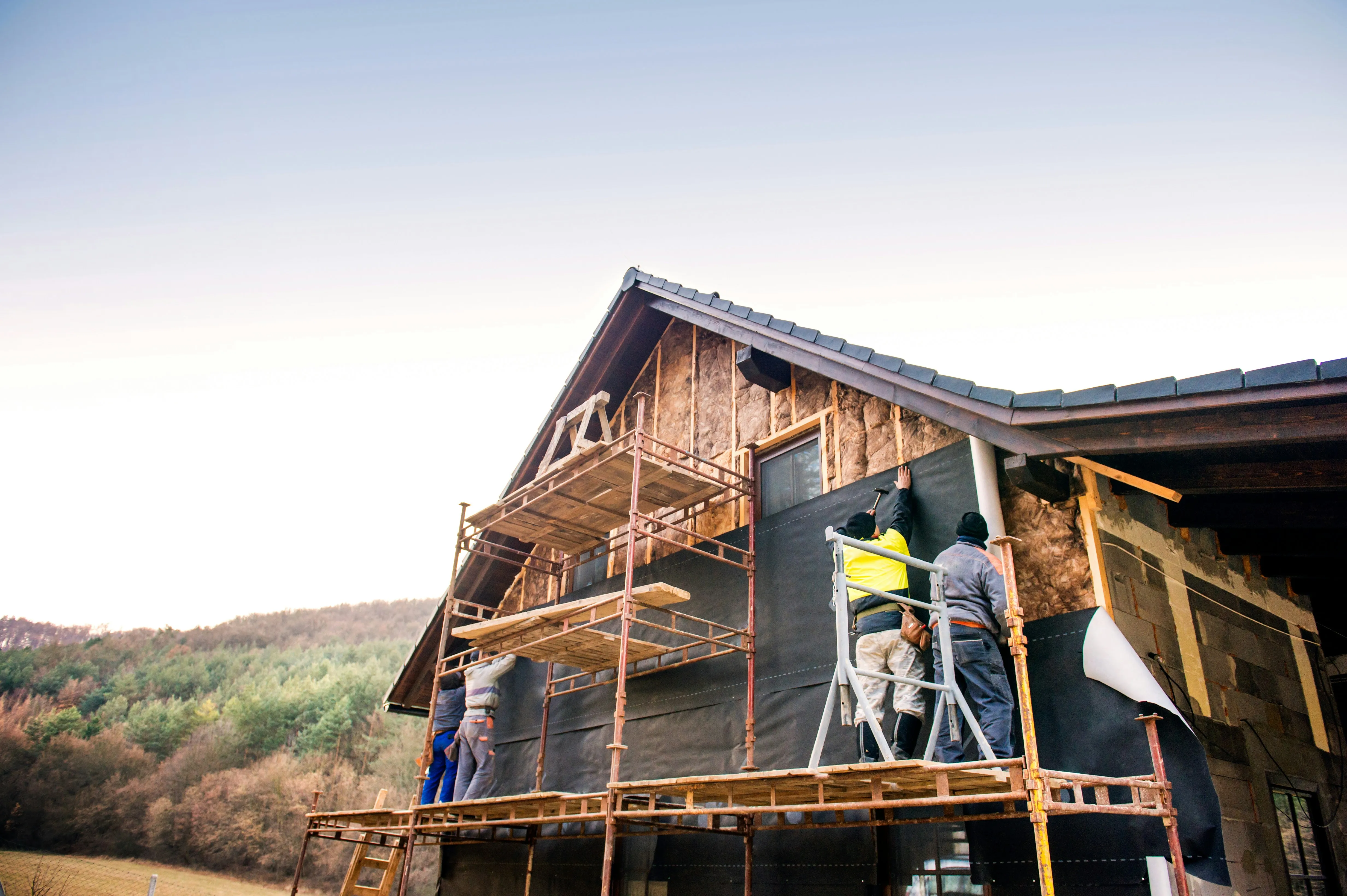 Structural repair crew on scaffolding working on an exterior wall — siding wrap and framing visible mid-project.