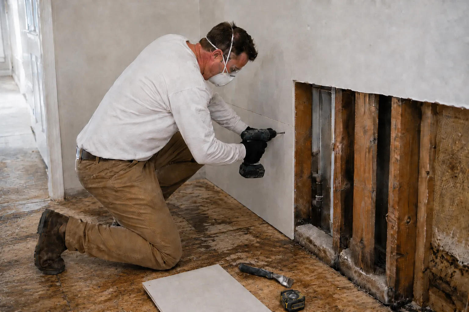 Water damage repair in progress — crew member in a respirator drilling new drywall back over exposed framing.